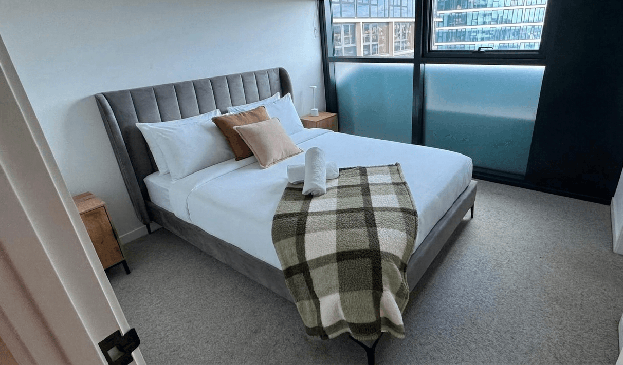Guest-ready Airbnb bedroom cleaned by Ventumm in Brisbane — hotel-style bed, fresh linen and rolled towels with city view